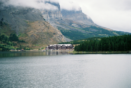 [In the foreground is a large expanse of water. The huge lodge looks like a tiny toy building compared to the mountains beside it and less than half the mountain height is in the photo.]